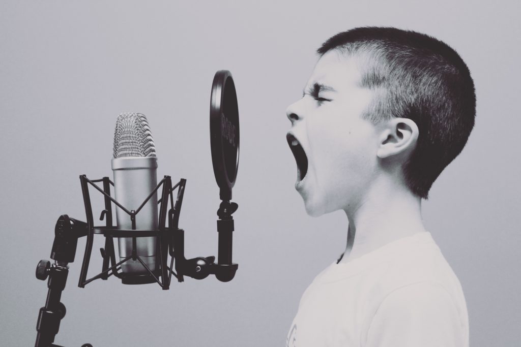 Boy communicating by screaming loudly into a microphone to represent bad virtual communication methods.